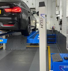 Black car on a vehicle lift in a professional garage workshop.