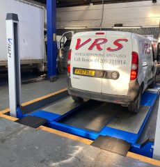 White van positioned on a wheel alignment system in a garage workshop.