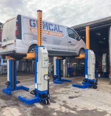 Commercial vehicle raised on mobile column lifts for maintenance.