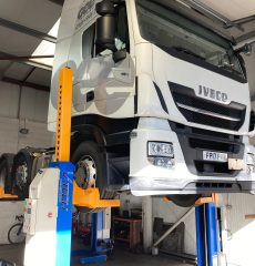 Four-column cabled vehicle lift for car servicing and maintenance in a professional garage.