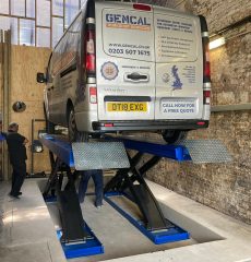 Commercial van undergoing vehicle inspection on a garage lift.