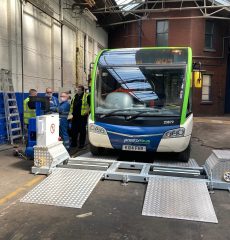 Bus undergoing vehicle inspection and testing in a workshop.